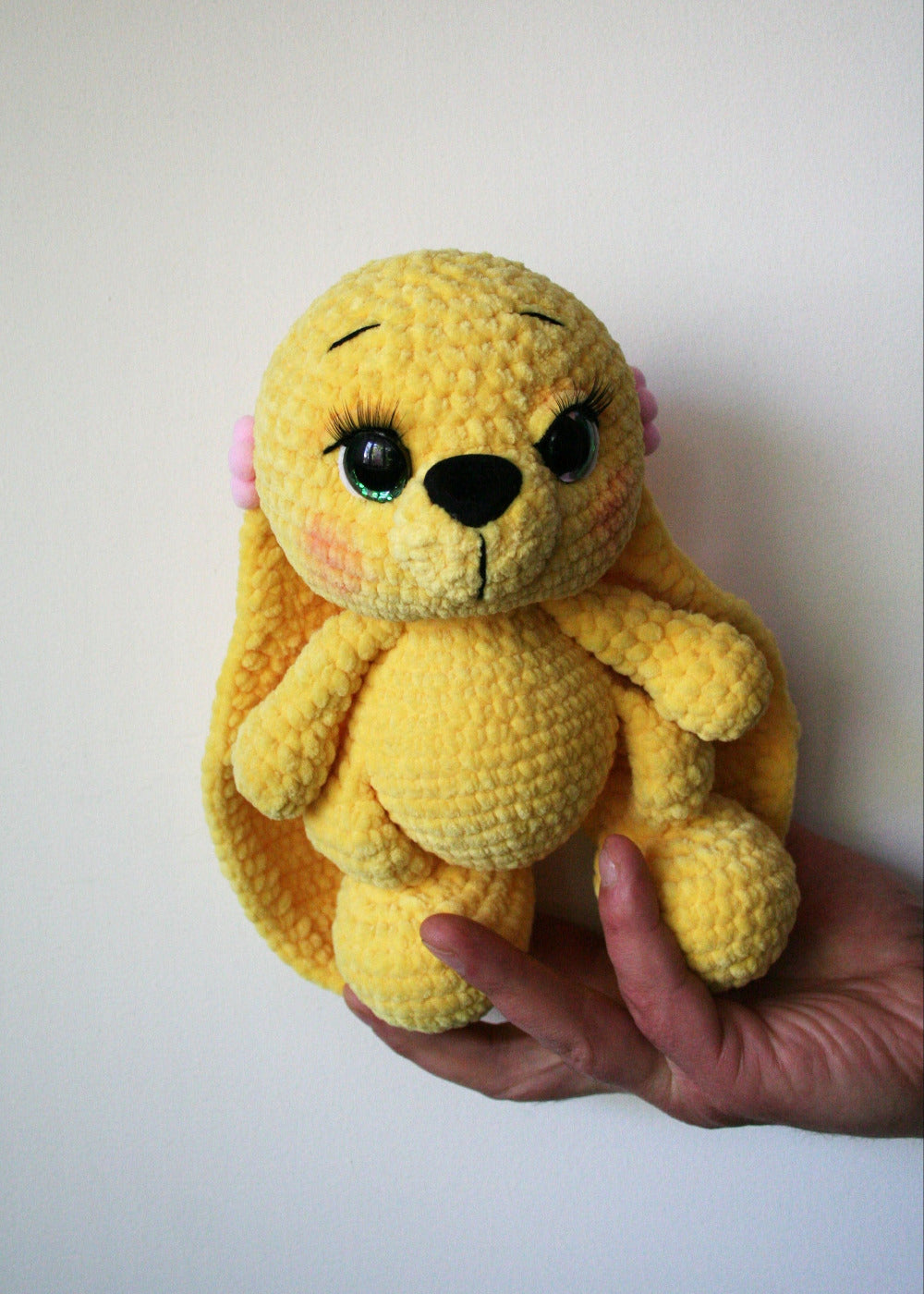 Close-up of crochet bunny face with safety eyes, glued eyelashes and safety nose, yellow plush yarn.