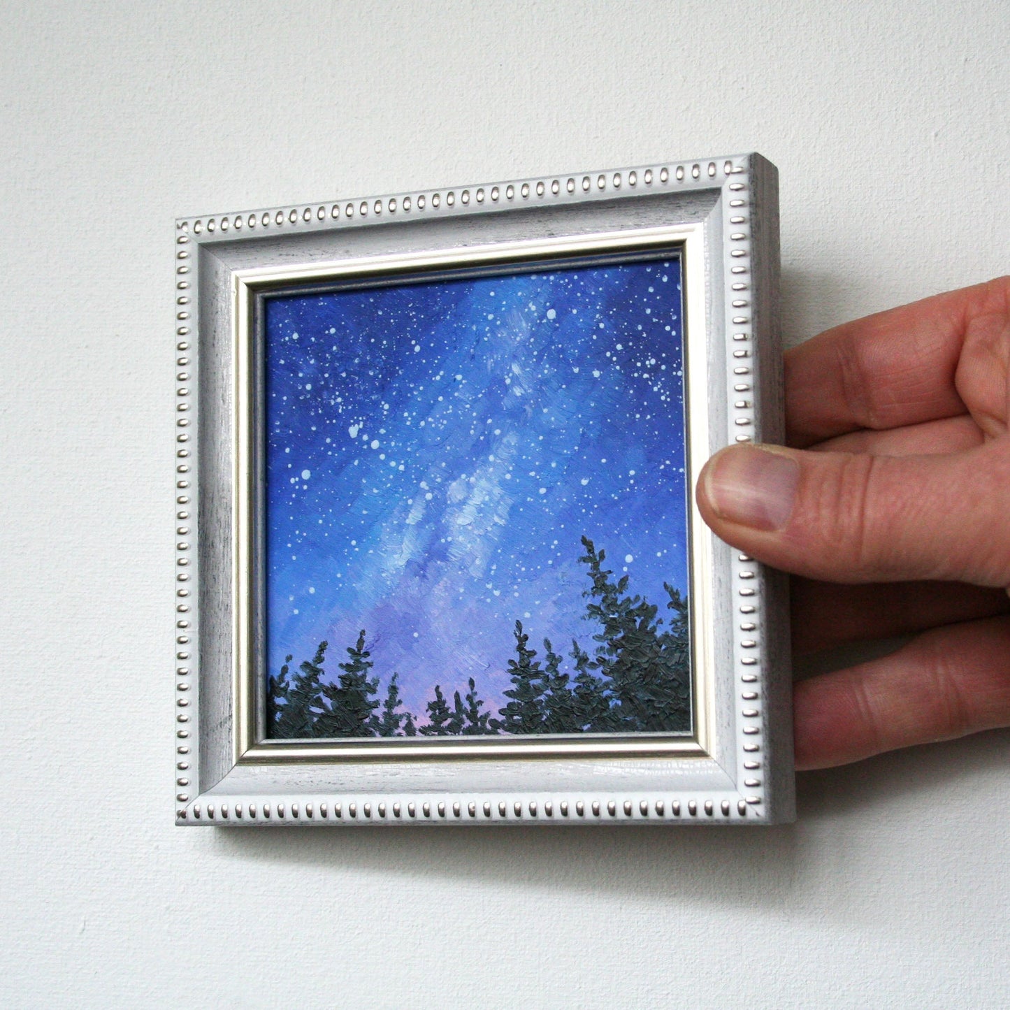 Framed artwork of a starry night sky with trees held by a hand 