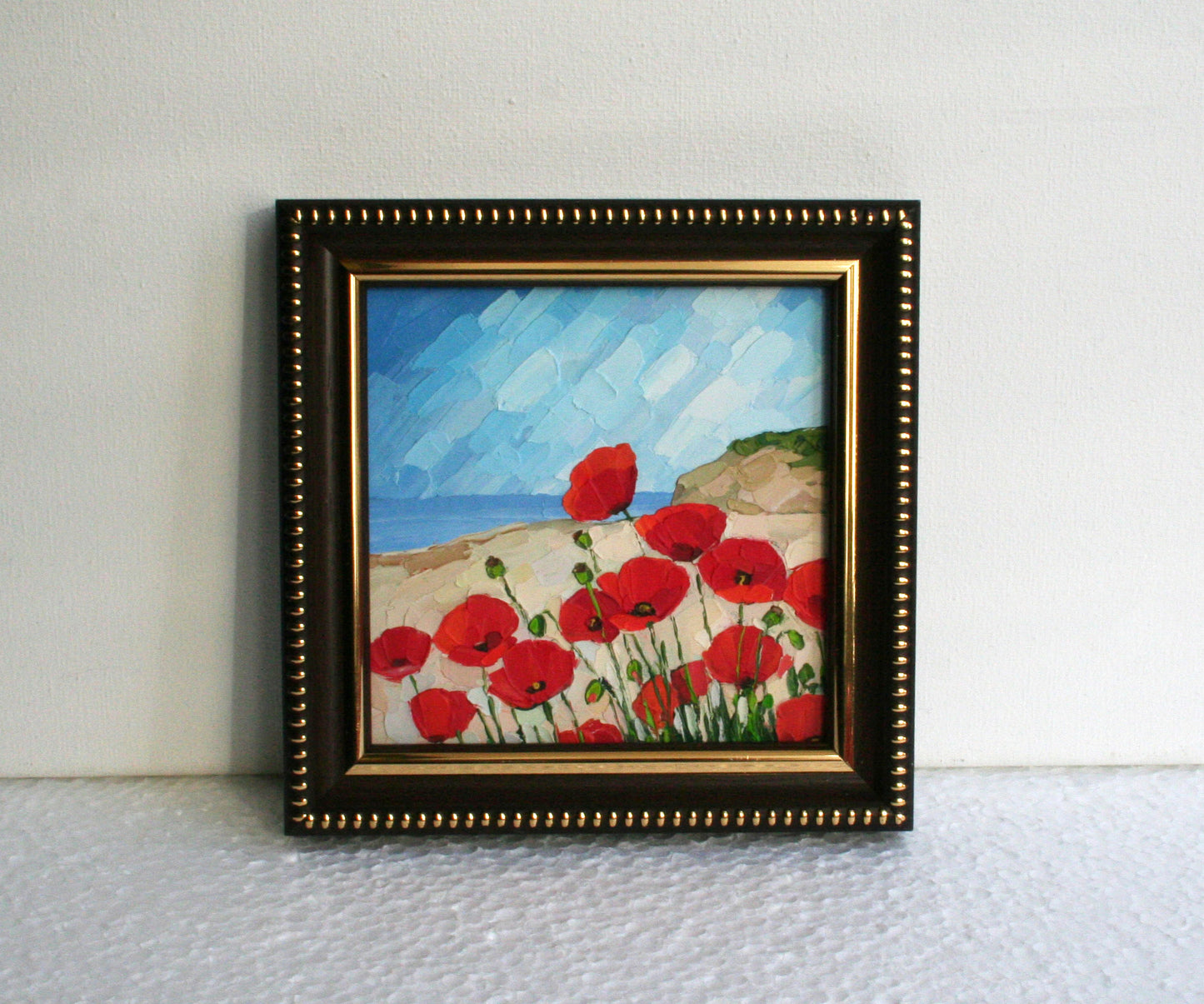 Framed painting of red poppies on a beach with a brown frame.