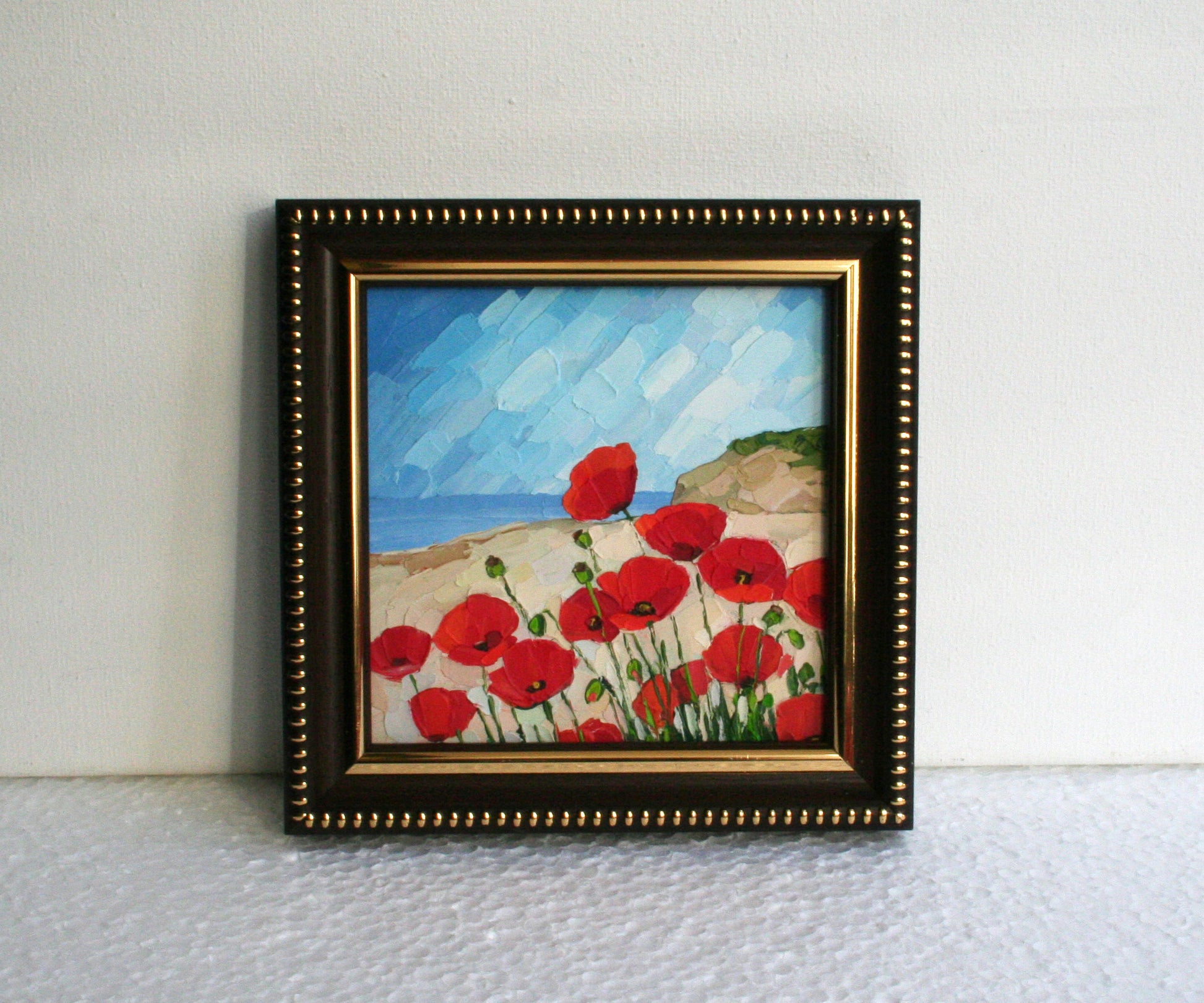 Framed painting of red poppies on a beach with a brown frame.