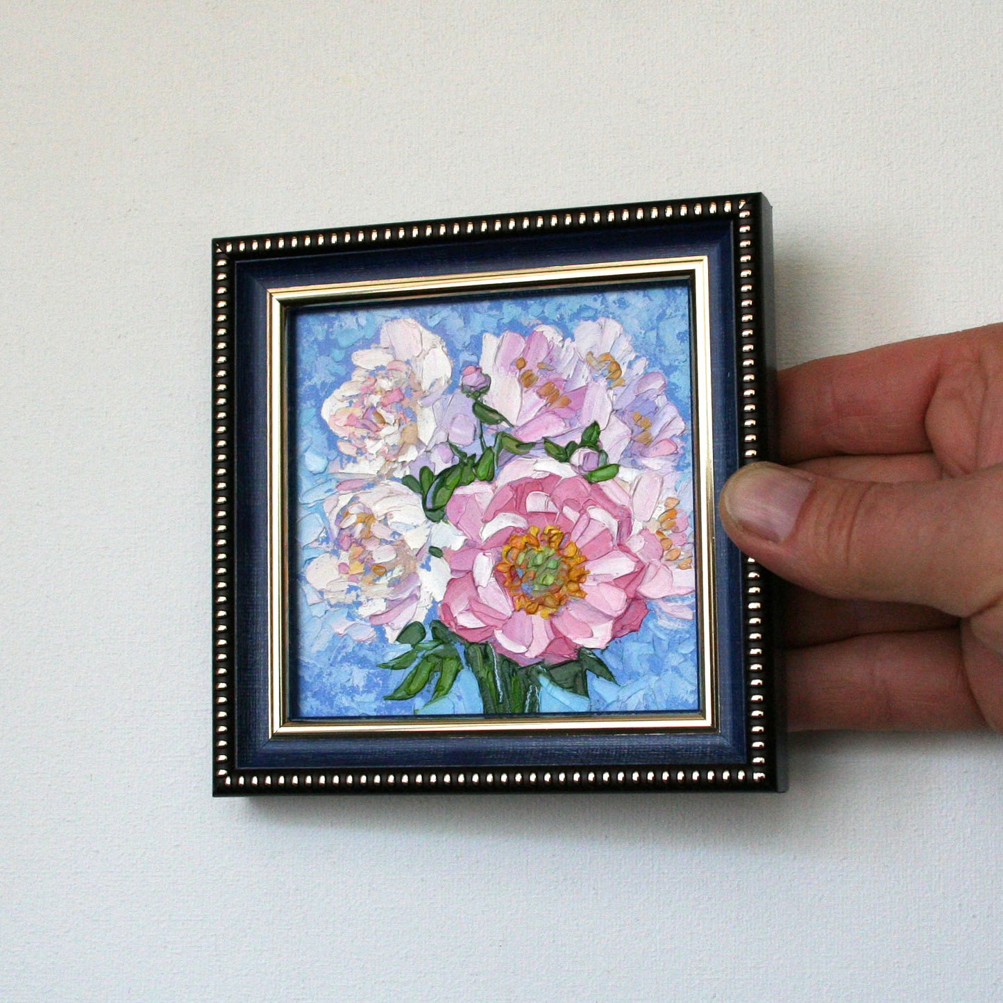 Small framed floral artwork held by a hand against a light background