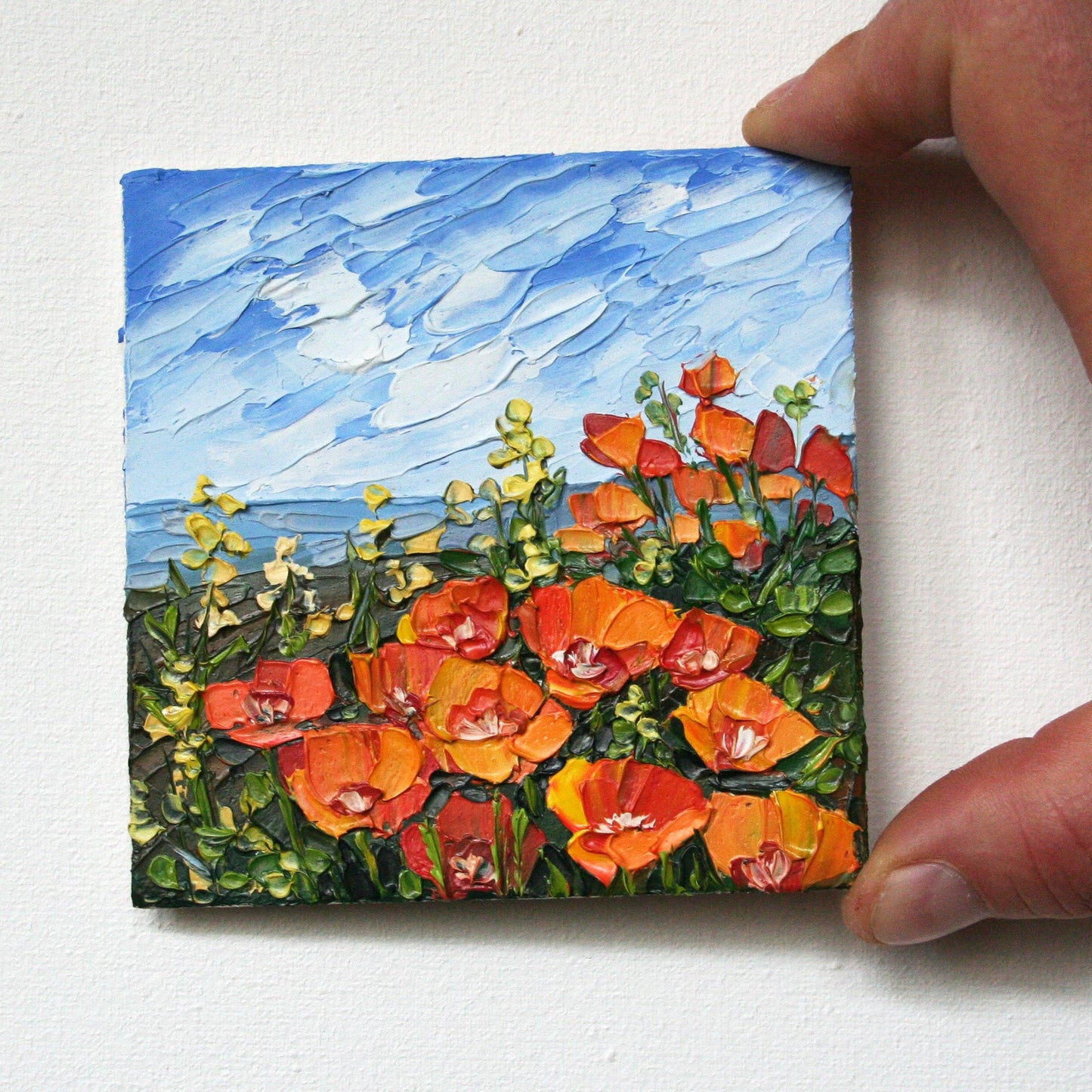 Small 4x4 inch California poppy painting held in hand, showing the miniature scale of the original oil art.