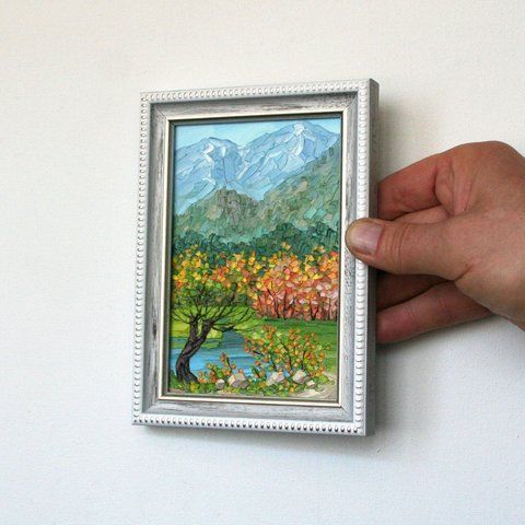 Small framed landscape painting of a mountain scene with trees and a lake.